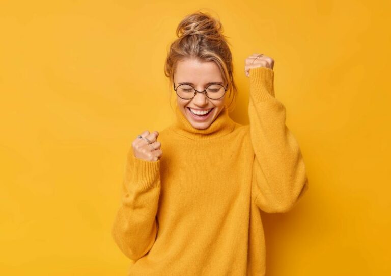 Woman in bright yellow cheering against yellow wall