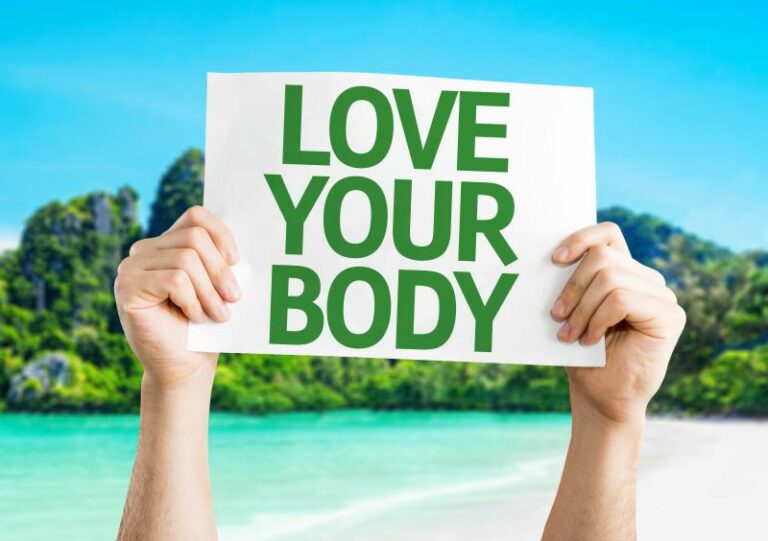 hands holding up love your body sign in front of tropical beach