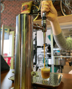 Hand pulling a nitro cold brewed tap pouring coffee