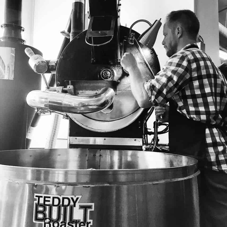 black and white photo of Cupper's coffee roaster with Josh checking a coffee sample
