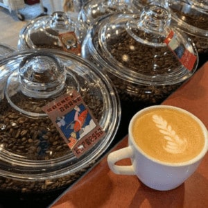 Latte art in white mug with Cupper's Coffee Jars behind