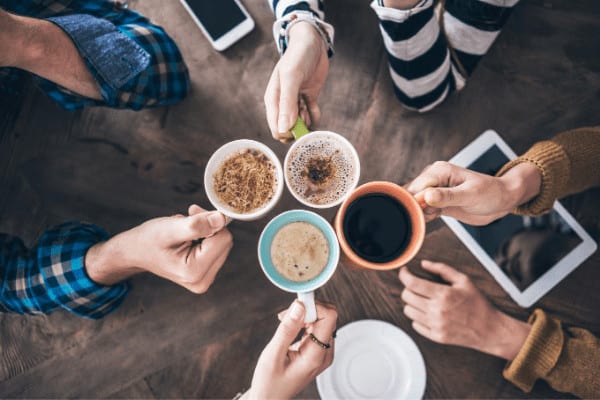 office coffee meeting, four mugs clinking together over a table