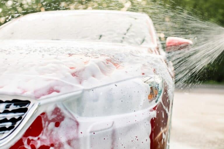 A bright red car covered in soap with water spraying on it from a hose, for fundraising