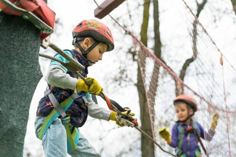 Two children wearing helmuts on a climbing netting outside