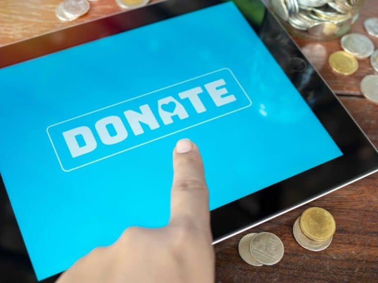 A fundraising tablet with blue screen featuring a Donate button with finger pressing it