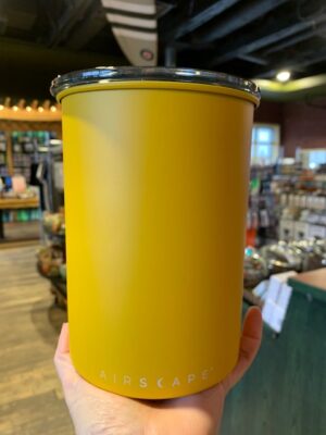 Hand holding a matte yellow metal tall Airscape canister with a smoked acrylic lid