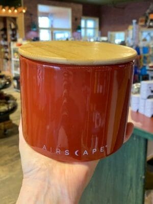 Hand holding a short ceramic red rock coloured Airscape canister with a bamboo lid