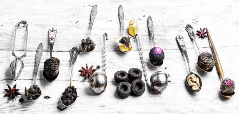 an assortment of spoons and tea balls with blooming tea and leaves on a white wood table