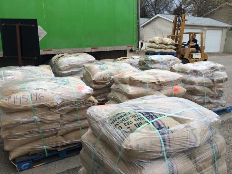 Pallets of bags of green coffee in front of a forklift and truck