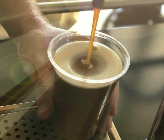 Nitro cold brewed coffee pouring from a tap into a plastic glass