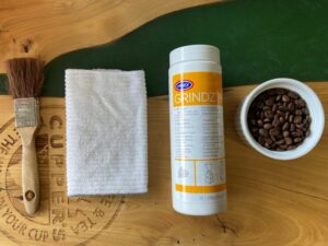 Brush, cloth, Urnex Grindz cleaner and coffee beans in a cup