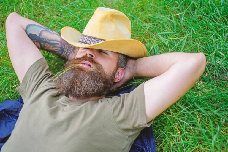 Man with tattoo and cowboy hat sleeping on grass