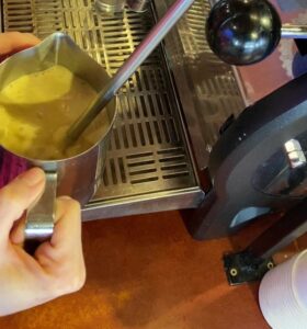 Steaming wand of an espresso machine frothing in milk pitcher