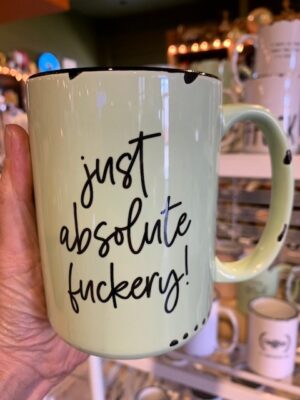 Hand holding green mug with "Just Absolute Fuckery" on it.