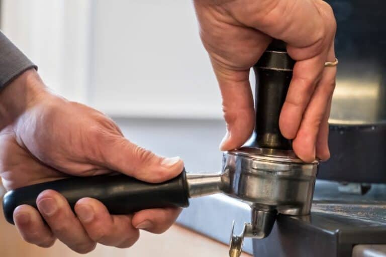 Hands pressing a shot with a tamper in a portafilter while using an espresso machine