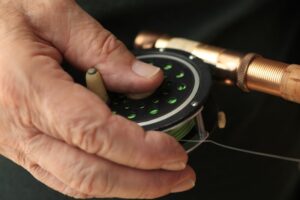 Older hand holding a fly fishing rod and reel.