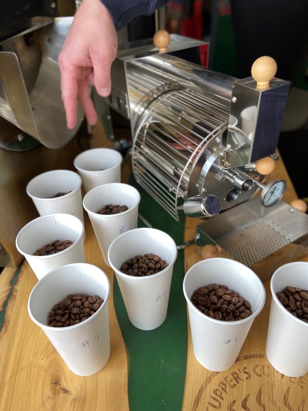 8 Cups of roasted coffee bean samples beside a mini-coffee roaster at Cupper's