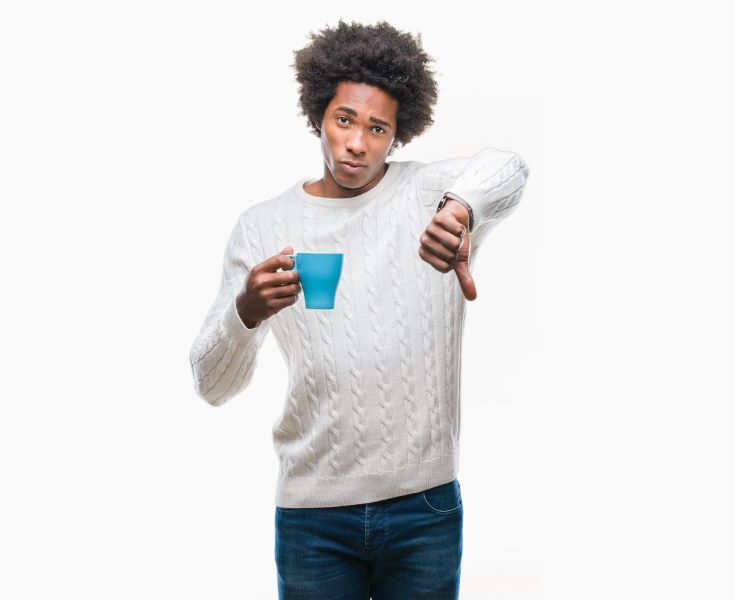 Man in white sweater holding a blue cup of coffee, thumbs down