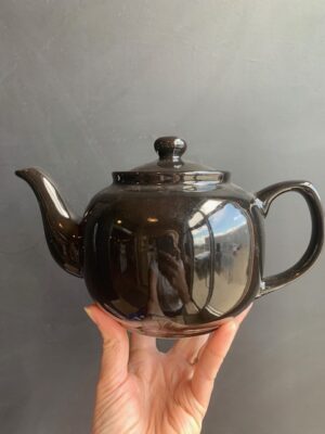 Black 6 cup Windsor Teapot being held up by a hand in front of a blackboard