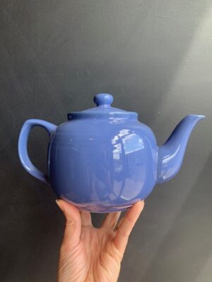 Blue 6 cup Windsor Teapot being held up by a hand in front of a blackboard