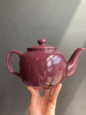 Burgundy 6 cup Windsor Teapot being held up by a hand in front of a blackboard