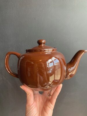 Dark Brown 6 cup Windsor Teapot being held up by a hand in front of a blackboard