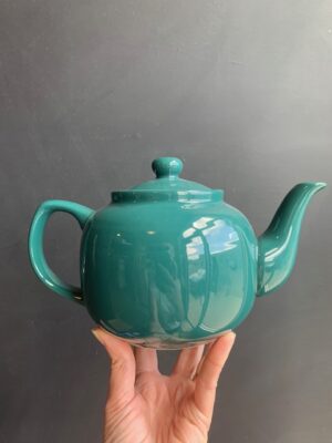 Green 6 cup Windsor Teapot being held up by a hand in front of a blackboard