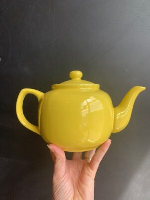 Lemon 6 cup Windsor Teapot being held up by a hand in front of a blackboard