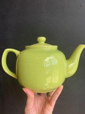 Tea Green 6 cup Windsor Teapot being held up by a hand in front of a blackboard