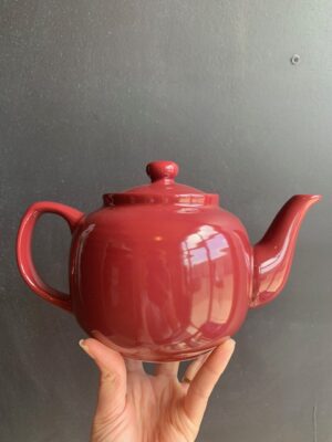 Vermillion Red 6 cup Windsor Teapot being held up by a hand in front of a blackboard