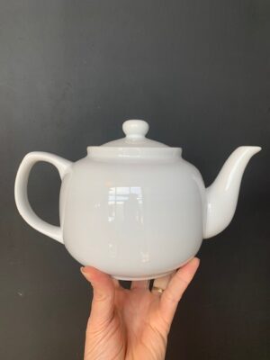 White 6 cup Windsor Teapot being held up by a hand in front of a blackboard