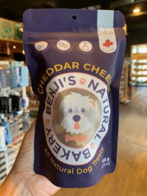 A small purple bag of Benji's Cheddar Cheese Dog Treats being held by a hand at Cupper's Coffee & Tea.