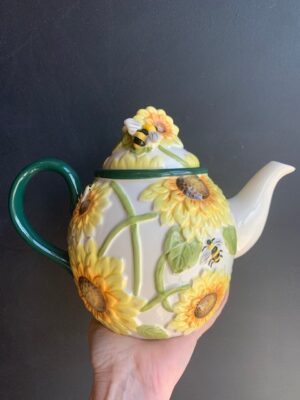 Sunflower Bee Teapot made by Blue Sky being held by a hand