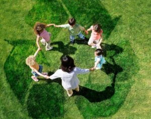 Children holding hands in a circle with a recycle emblem in the grass at their feet