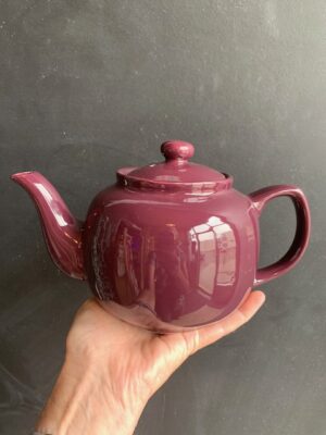 Plum 6 cup Windsor Teapot being held up by a hand in front of a blackboard