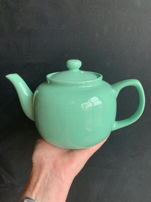 Sea Foam 6 cup Windsor Teapot being held up by a hand in front of a blackboard