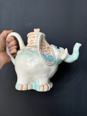 a hand holding a Blue Sky Clayworks White Elephant Teapot