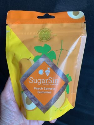 SugarSin Peach Sangria Gummies in a yellow & peach bag being held by a hand