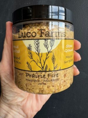 Luco Farms Prairie Fire mustard in a plastic jar, being held by a hand