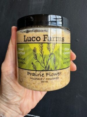 Luco Farms Prairie Flower mustard in a plastic jar, being held by a hand