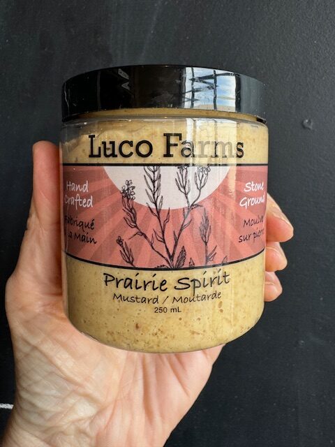 Luco Farms Prairie Spirit mustard in a plastic jar, being held by a hand