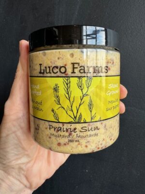 Luco Farms Prairie Sun mustard in a plastic jar, being held by a hand