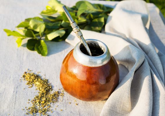 a yerba mate gourd and bombilla with leaves on a white cloth