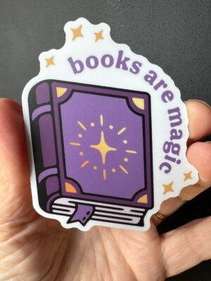 Hand holding a sticker with a purple book and the words "Books are Magic"