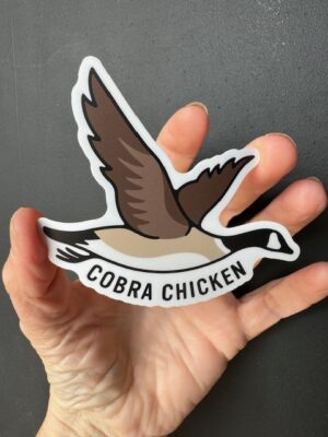 Hand holding a sticker with a flying Canada Goose and the words "Cobra Chicken"