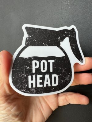 Hand holding a sticker with a full coffee carafe and the words "Pot Head"