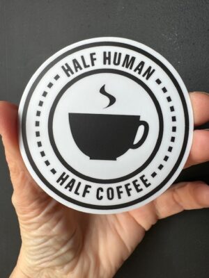 Hand holding a sticker with a steaming cup, and words 'Half Human, Half Coffee' above and below the cup.