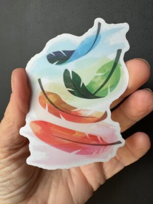 Hand holding a sticker with four pastel coloured feathers drifting down it