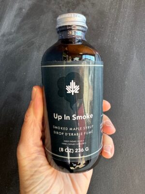 a hand holding a bottle of Dript Up In Smoke Maple Syrup