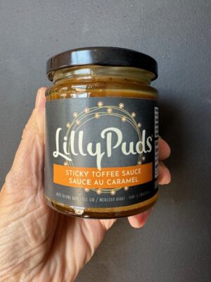 a hand holding a jar of LillyPud's Sticky Toffee Sauce